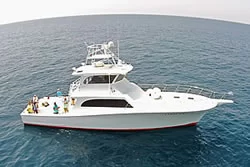 A white yacht with a red stripe is floating on calm blue ocean water. Several people are on the deck, enjoying the view and relaxing under partly cloudy skies.